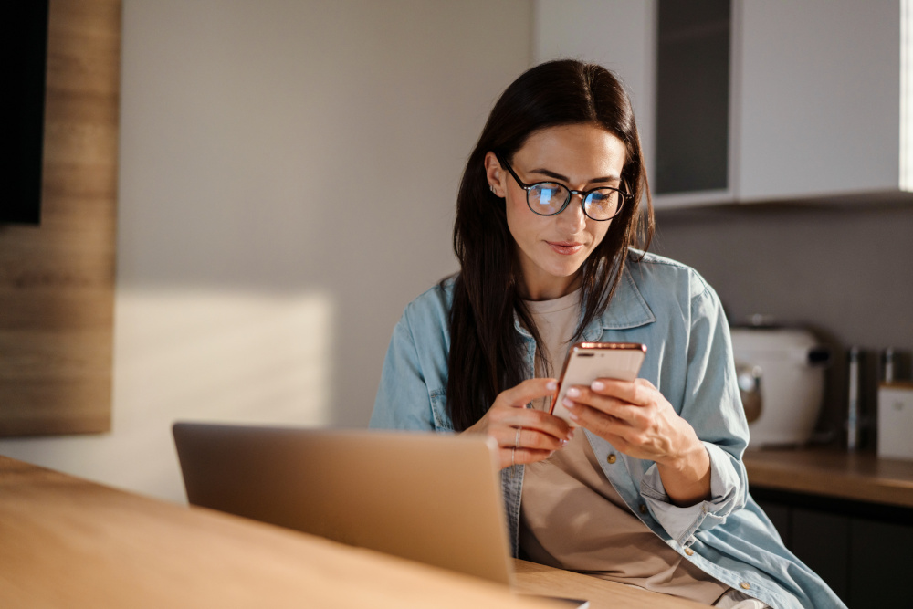 Eine Frau sitzt am Schreibtisch und schaut auf ihr Smartphone